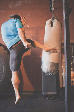 Muscular man practices a powerful kick on a heavy bag