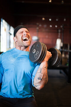 Tattooed man yelling during an intense dumbbell curl