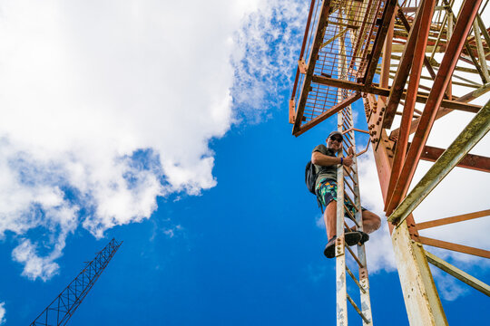 A smiling man climbs a tall rusty tower
