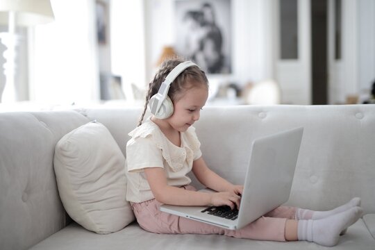 Young girl with headphones using a laptop on the couch