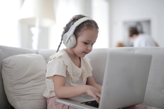 Little girl with headphones using laptop at home