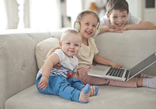 Three happy siblings smiling on the couch with a laptop
