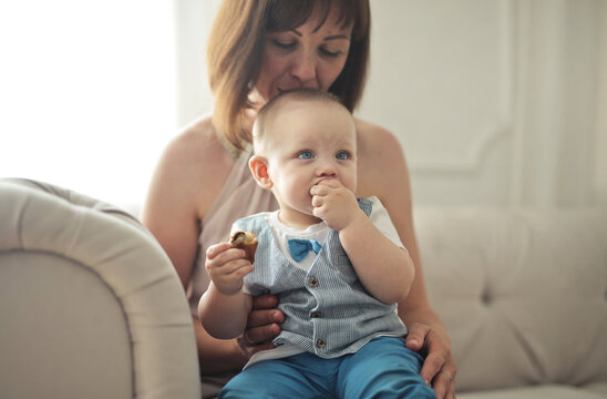 Mother kisses her cute baby boy eating a snack