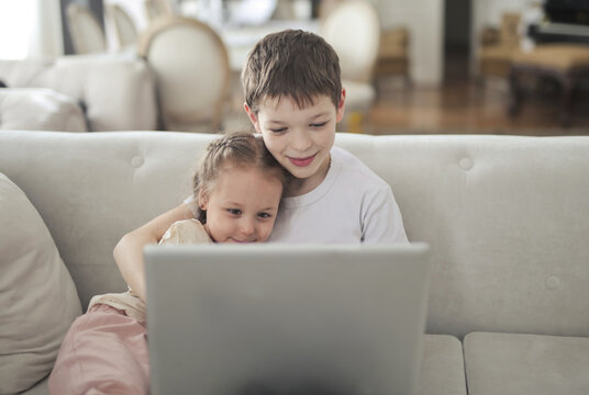 Brother and sister cuddling on couch watching laptop