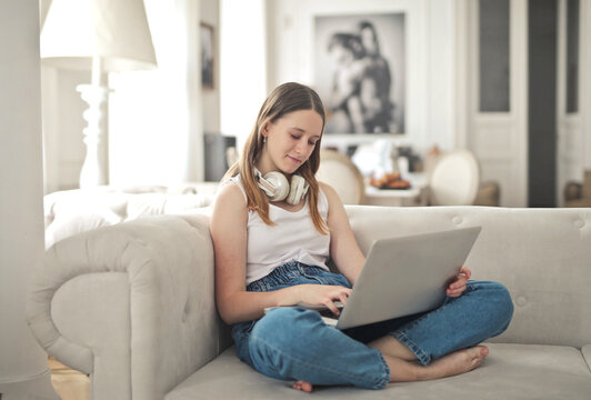 Young woman with headphones using a laptop on sofa
