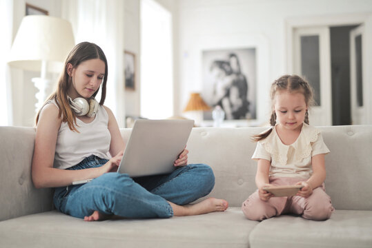 Two sisters on a couch using their electronic devices