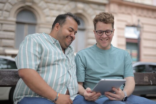 Two male friends laughing at a tablet outside