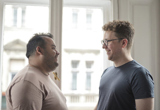 Two diverse male friends talking together by a window