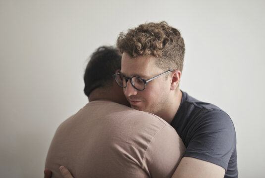 Man with glasses comforts his friend with a hug