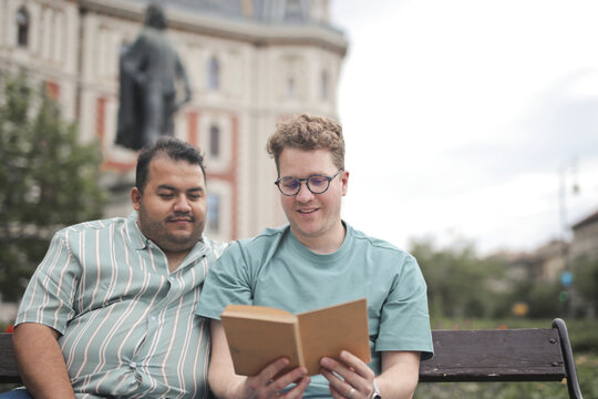 Male couple enjoys a book together on a park bench