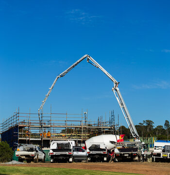 tradies utes parked beside worksite with concrete pump machine towering over scaffolding