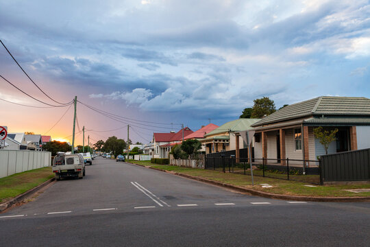 Sunset light peeking from behind clouds down residential road in country town of Singleton