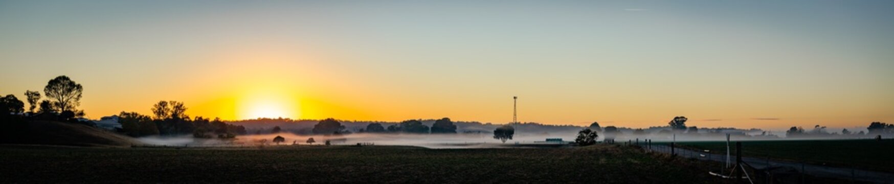 Rural farm landscape scene with mist ribbons settled over distant paddocks at dawn