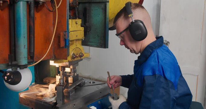 Skilled blue collar worker operating punch press in factory. Industrial labor in metal parts manufacturing