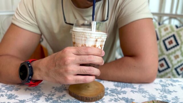 Young Man Enjoys a Refreshing Iced Coffee Drink at a Cozy Cafe Table