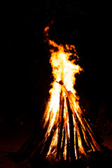 Tall teepee bonfire with bright flames burning against dark night © Ionut Gaspar
