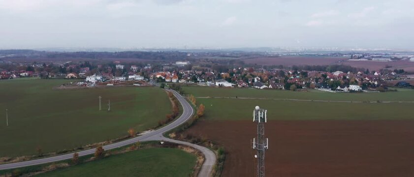 Aerial drone perspective of a tall telecommunications cell tower standing beside empty country roads agricultural fields and a small town