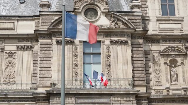 French flag waves on pole outside Louvre palace building in Paris France. National tricolor banner concept for european politics government news and french state holiday celebration.