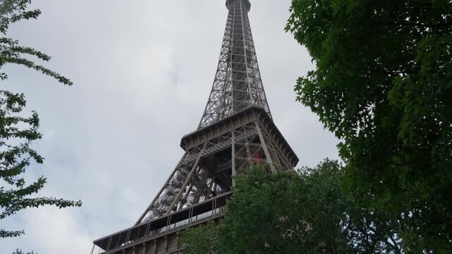 Eiffel tower historic steel architecture monument stands under overcast sky in France. Cloudy rainy weather provides moody background for european travel industry and tour marketing.