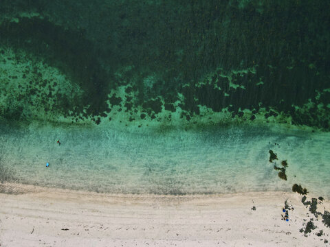 Aerial view of Talisker Bay Beach featuring turquoise water, dark seaweed patches, and people on the white sand in Isle of Skye, United Kingdom.
