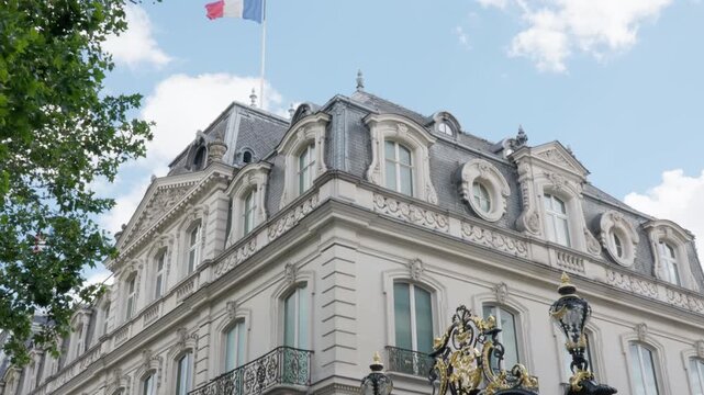 French flag waves on top of luxury palace architecture building facade with gold wrought iron gate in Paris France. Historic real estate landmark serves for diplomacy governance and tourism.