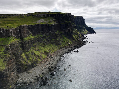 Aerial view of the dramatic dark cliffs and rocky shoreline of Talisker Bay Beach under a cloudy sky in Isle of Skye, United Kingdom.