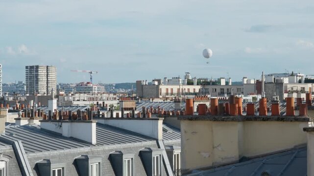 Haussmann architecture buildings feature traditional Parisian rooftops and terracotta chimney pots with an air balloon floating in the sky over Paris France. Urban residential real estate scene.