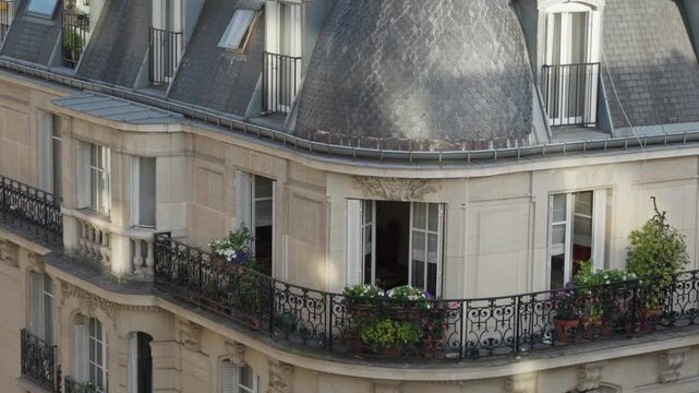 Haussmann architecture apartment building balcony with wrought iron railing and blooming flower pots features open windows in Paris France. French residential real estate exterior scene.