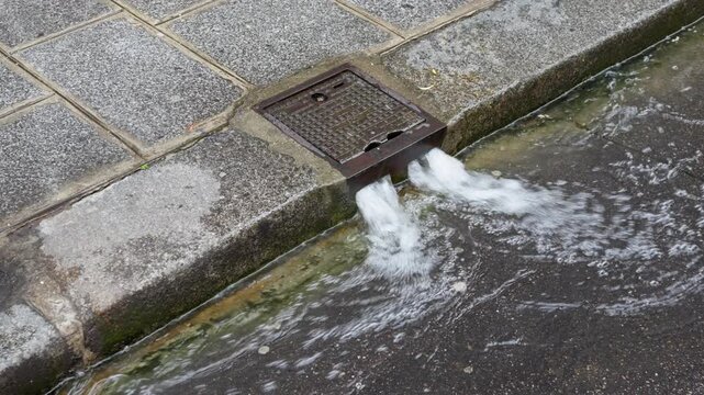 Water flows from a Paris street washing bouche de lavage system onto asphalt pavement. Municipal non-potable water network handles urban sanitation, sidewalk cleaning and public service.