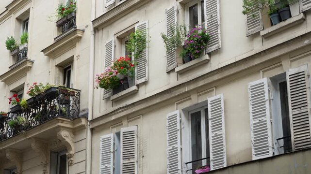 Parisian residential apartment building facade features classic windows with open wooden shutters and flower boxes. French architecture exterior represents European real estate and tourism.