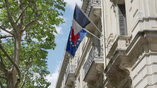 France national tricolor flag and European Union flag flutter on a stone building facade in Paris. French government administration house represents diplomacy, patriotism and state politics.