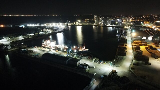 Aerial view of the illuminated harbor at night with docked cargo ships, industrial warehouses, and bright dockside lighting in Chatham, England, United Kingdom.