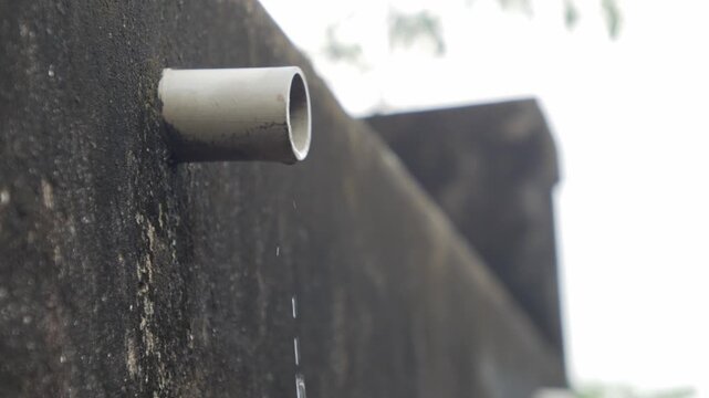 PVC pipe protruding from dark mossy concrete wall with water dripping drops leaking drainage outdoor urban detail