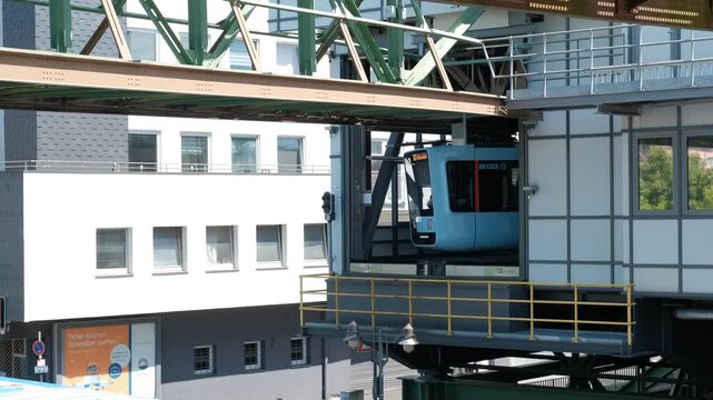 Germany, Wuppertal, June 20 2025. Close up shot of a blue hanging monorail train car arriving at a public transport terminal station in a European city.