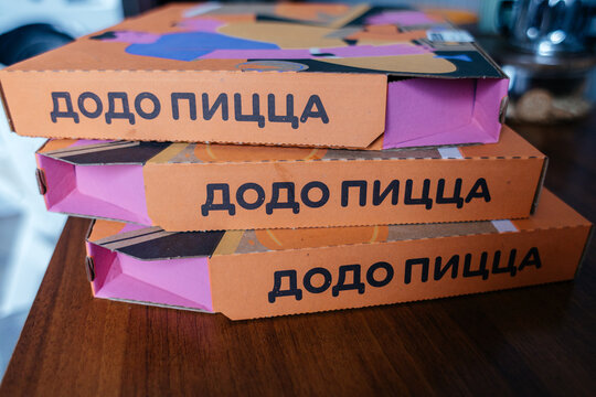 Three stacked pizza boxes with colorful designs and the text 'DODO Pizza' prominently displayed. The boxes are placed on a wooden surface.