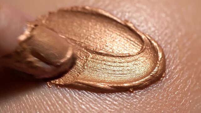 Close up of bronze metallic makeup cream applied on skin with finger showing smooth texture and shimmer