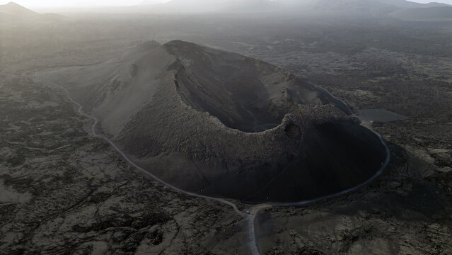 Aerial view of the volcanic crater in Lanzarote, featuring rugged dark lava fields and dramatic geological formations under soft light in Lanzarote, Canarias, Spain.