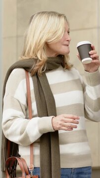 Vertical video: Sipping coffee woman in striped top and scarf, taking paper bag from friend outside
