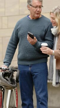 Vertical video: Showing phone, pair in sweater, coat walking city street sharing with bike, coffee