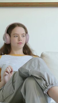 Vertical video: Song starting, woman in mustard sleeves and pink headphones tapping along on sofa