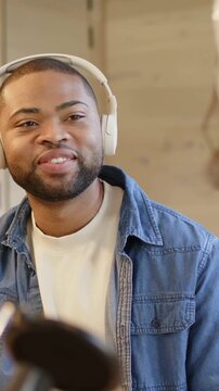 Vertical video: Smiling host in denim jacket responding to cohost laugh into mics in podcast studio