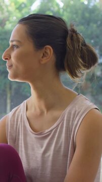 Vertical video: Hearing offscreen voice woman in pale top plum leggings turning near window smiling