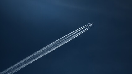 Airplane high in dark blue sky with long white streaks of exhaust fumes behind it © lucia2311