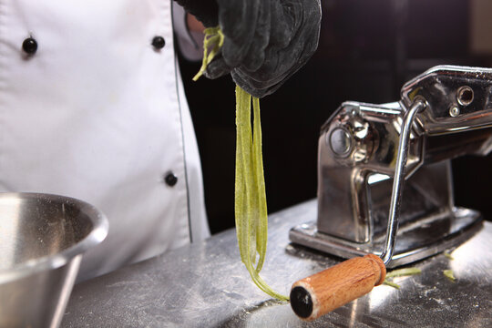 Chef prepares dough with spinach. Homemade pasta. Machine for making pasta and rolling out dough. Cooking pasta with spinach