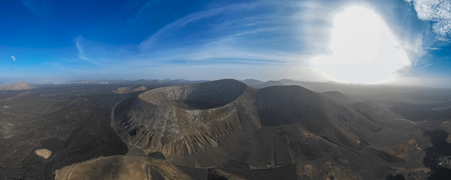 Aerial view of the volcanic crater landscape with rugged terrain and dramatic shadows under a bright blue sky in Lanzarote, Canarias, Spain.