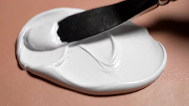 Close up of white paint being spread on a smooth surface with a metal palette knife