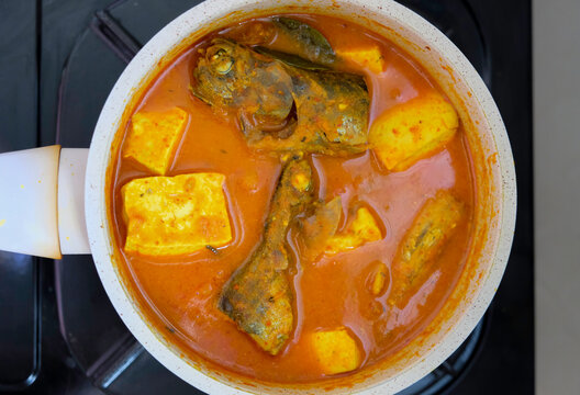 Overhead view of asam pedas fish and tofu stew cooking in a pan on a stovetop