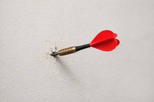 A red dart is stuck in a wall with a hole, suggesting an attempt to stick the dart into something but failed