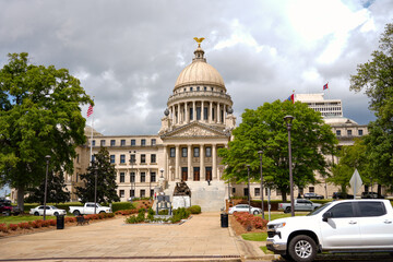 Obraz premium Mississippi State Capitol building from street level with vehicles trees and dramatic stormy sky