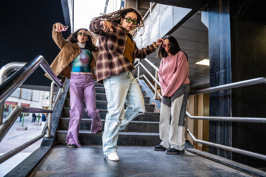 Gen-Z women friends dancing on city stairs in streetwear